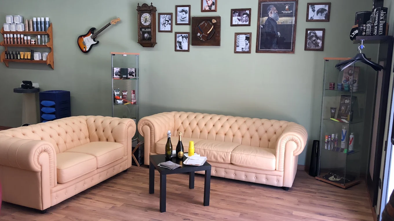 La sala d'attesa del barbershop: due divani chesterfield color crema, parete verde salvia con foto d'epoca e una chitarra elettrica appesa