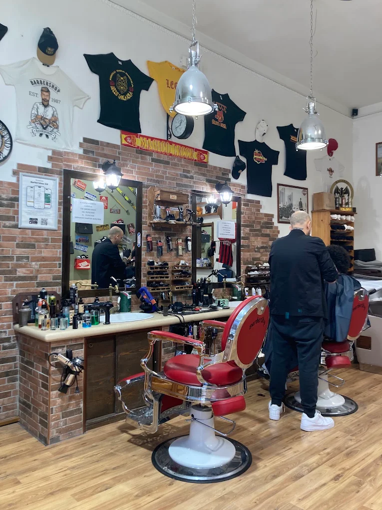 L'interno del Barbershop di Alessio Maggio: due poltrone da barbiere rosse davanti agli specchi e alla parete in mattoni